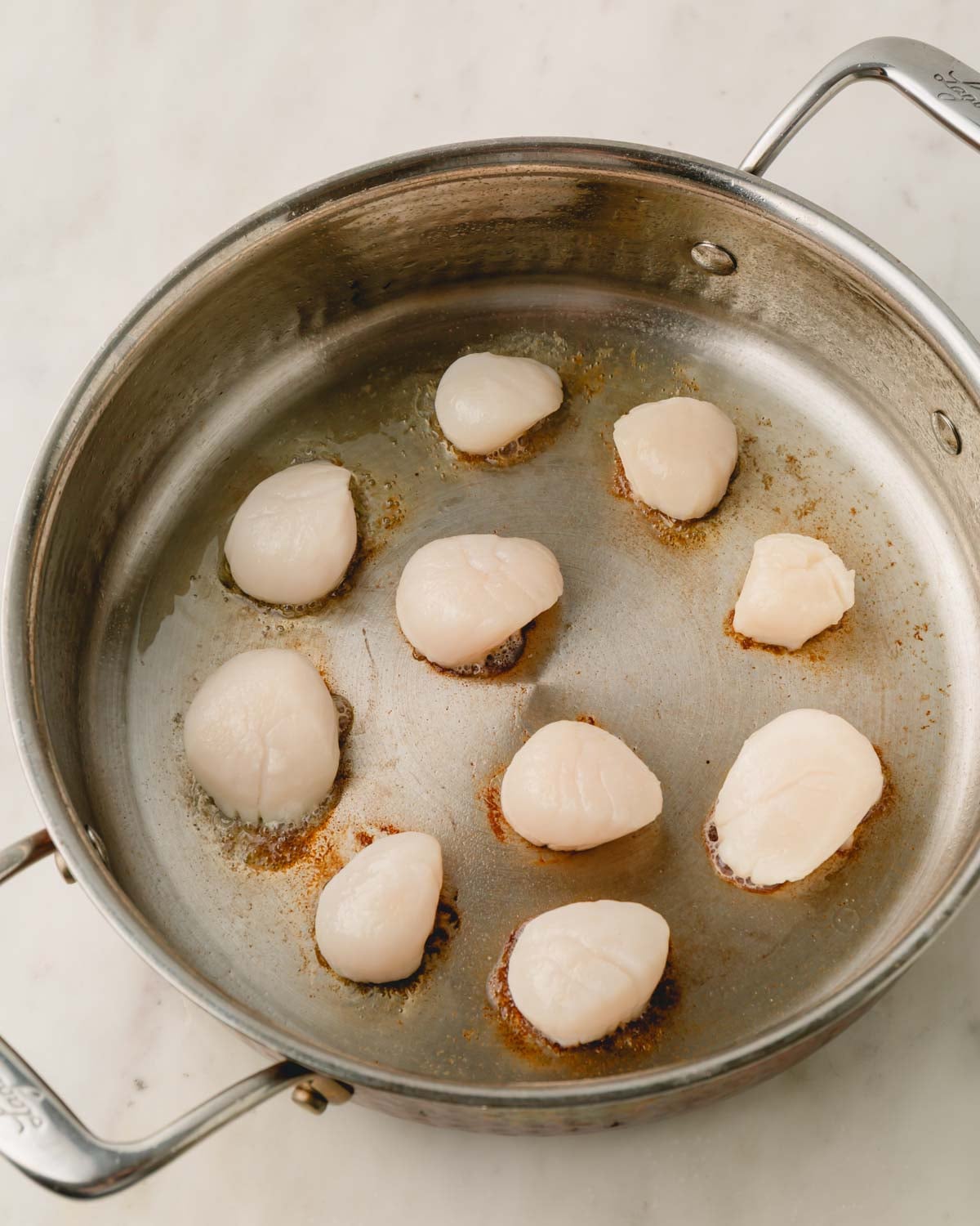 Scallops being searing in a pan.