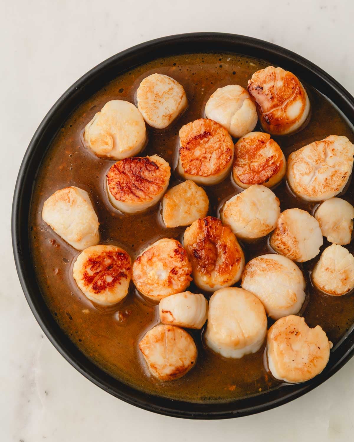 Scallops on a black plate with white wine sauce.