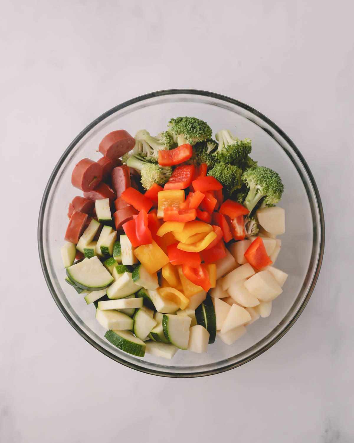 A glass bowl with sausage and vegetables.