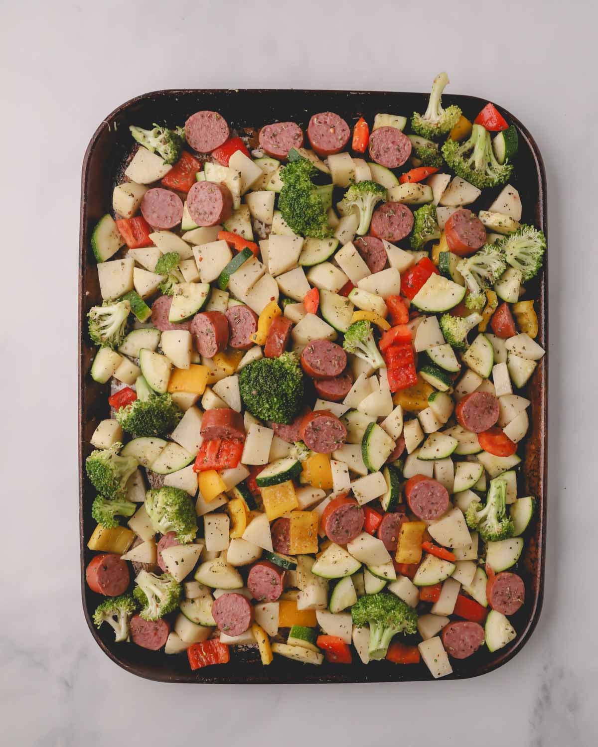 A sheet pan with sausage and vegetables before baking.