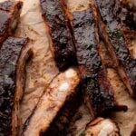 St. Louis style ribs in the oven cut on a piece of parchment paper with a white bowl of sauce.