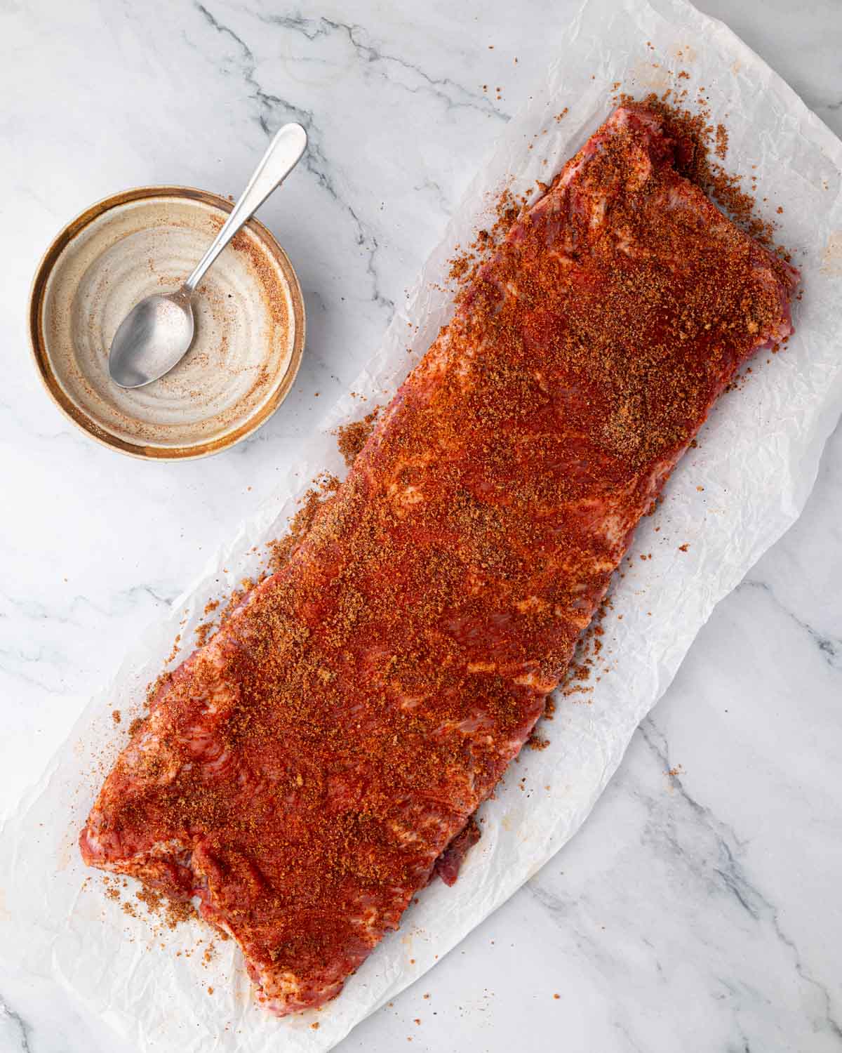 St. Louis-style ribs with a spice rub on them. An empty cream bowl and a spoon are to the side.