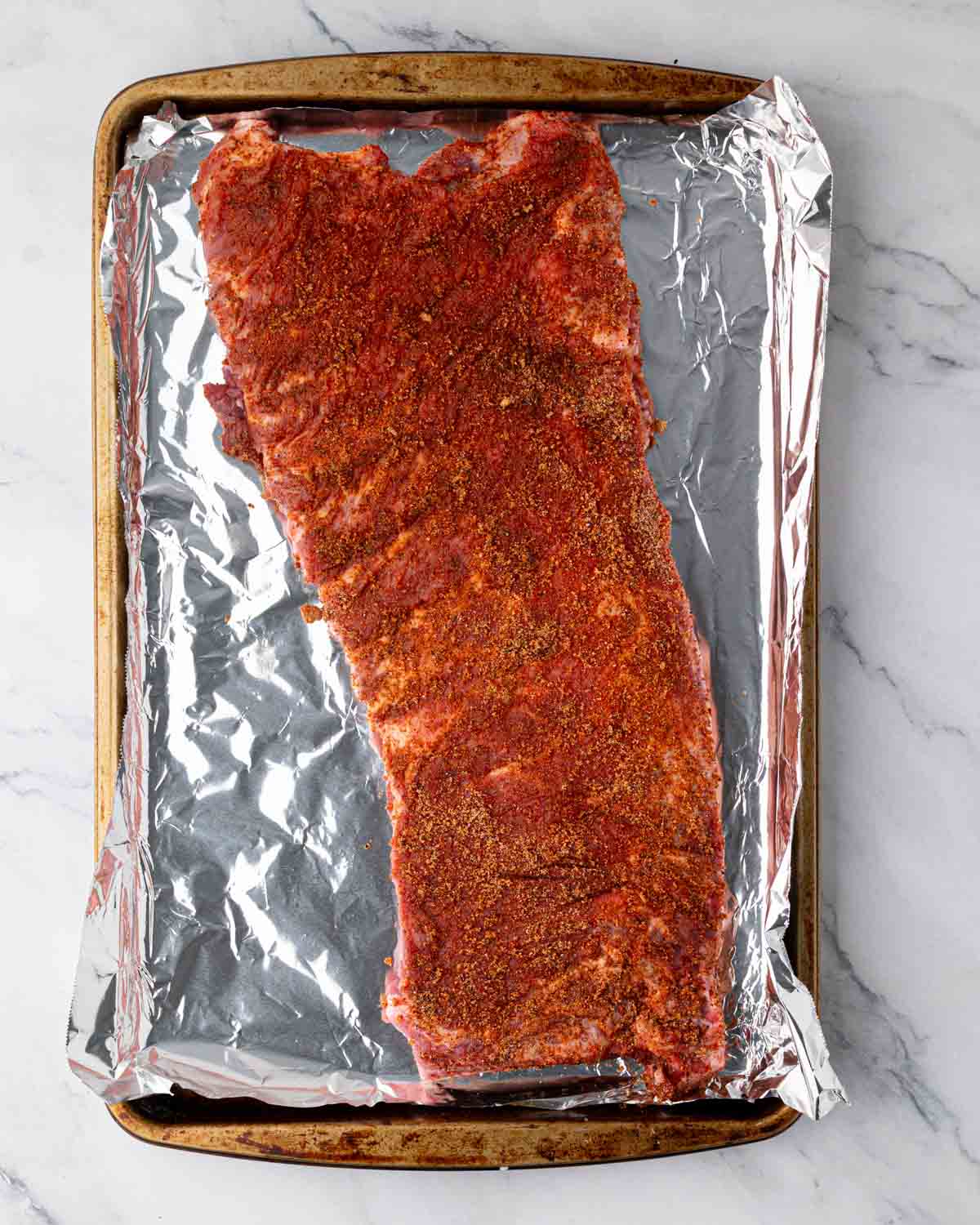 A baking sheet lined with foil with spice-rubbed St. Louis ribs ready to bake.