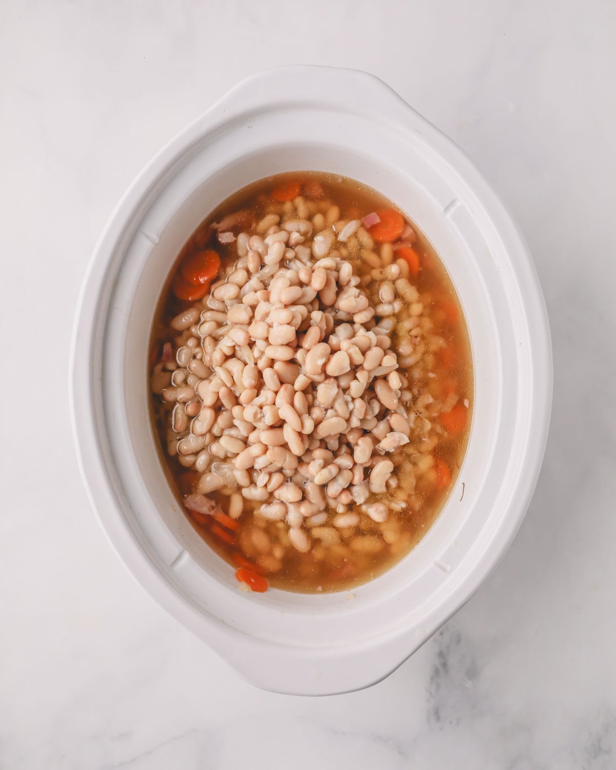 A white slow cooker with ham and beans ingredients.