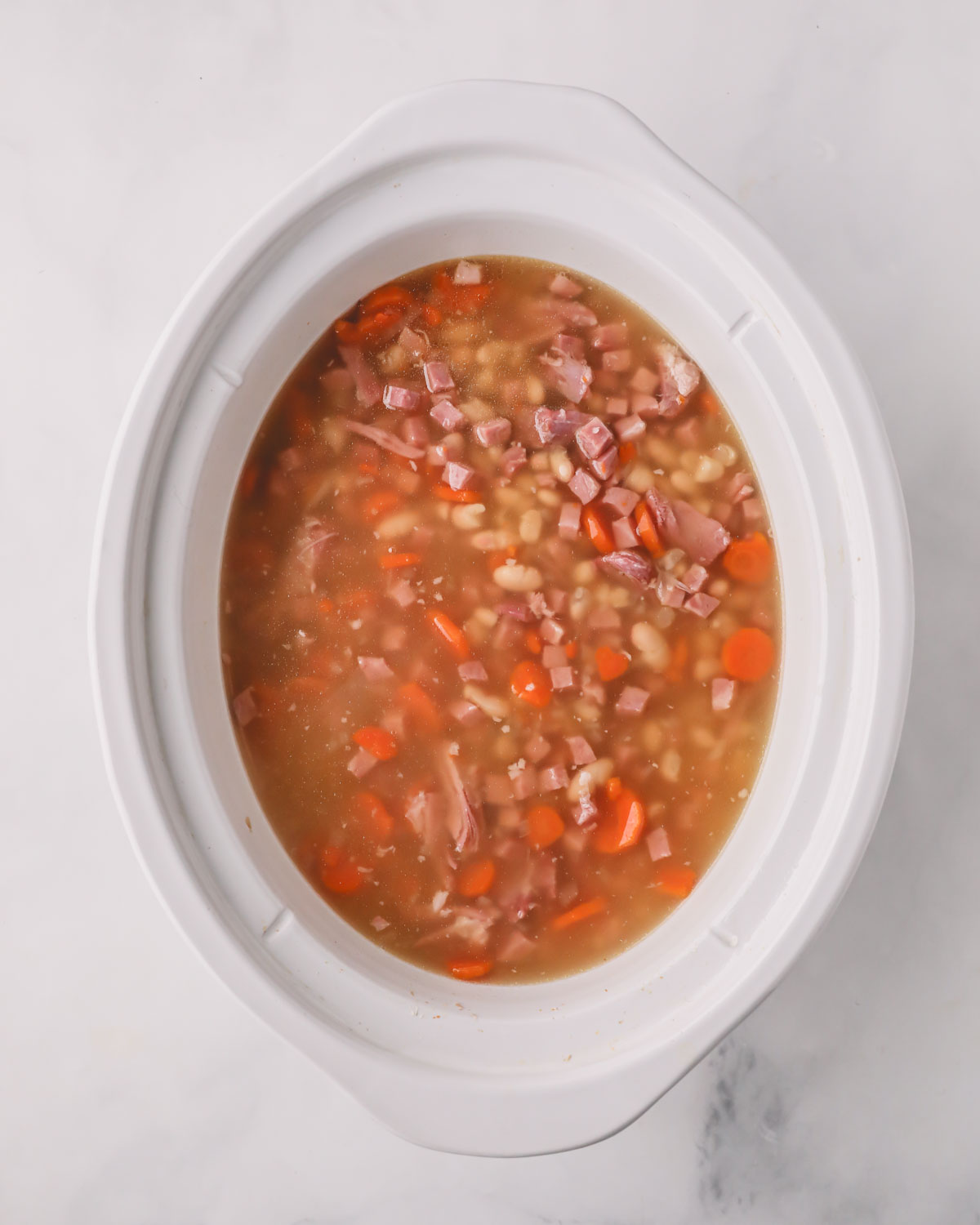 A white slow cooker with ham and beans.