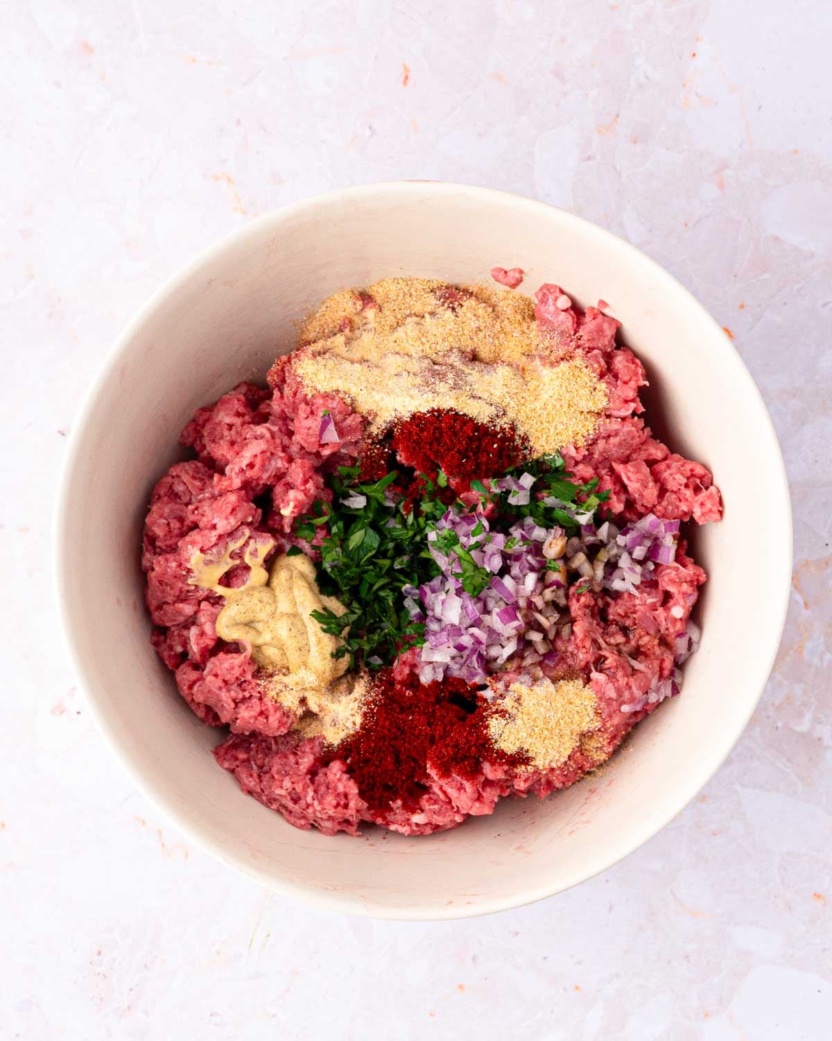 A white bowl with ground bison meat and seasonings.