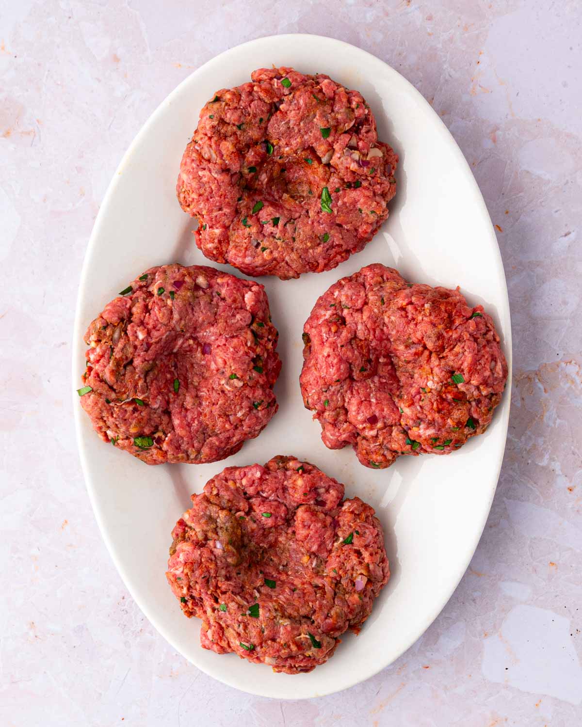 A white platter with shaped bison burger patties before grilling.