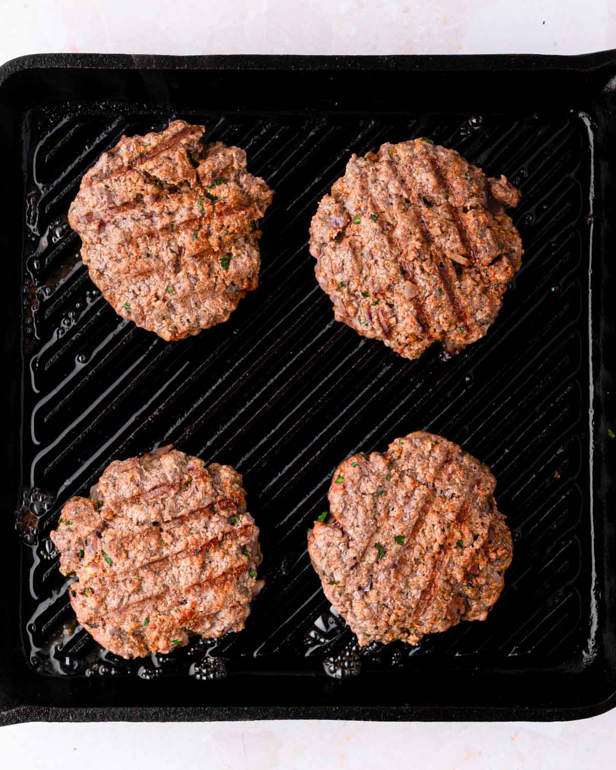 A grill pan with bison burgers cooking.