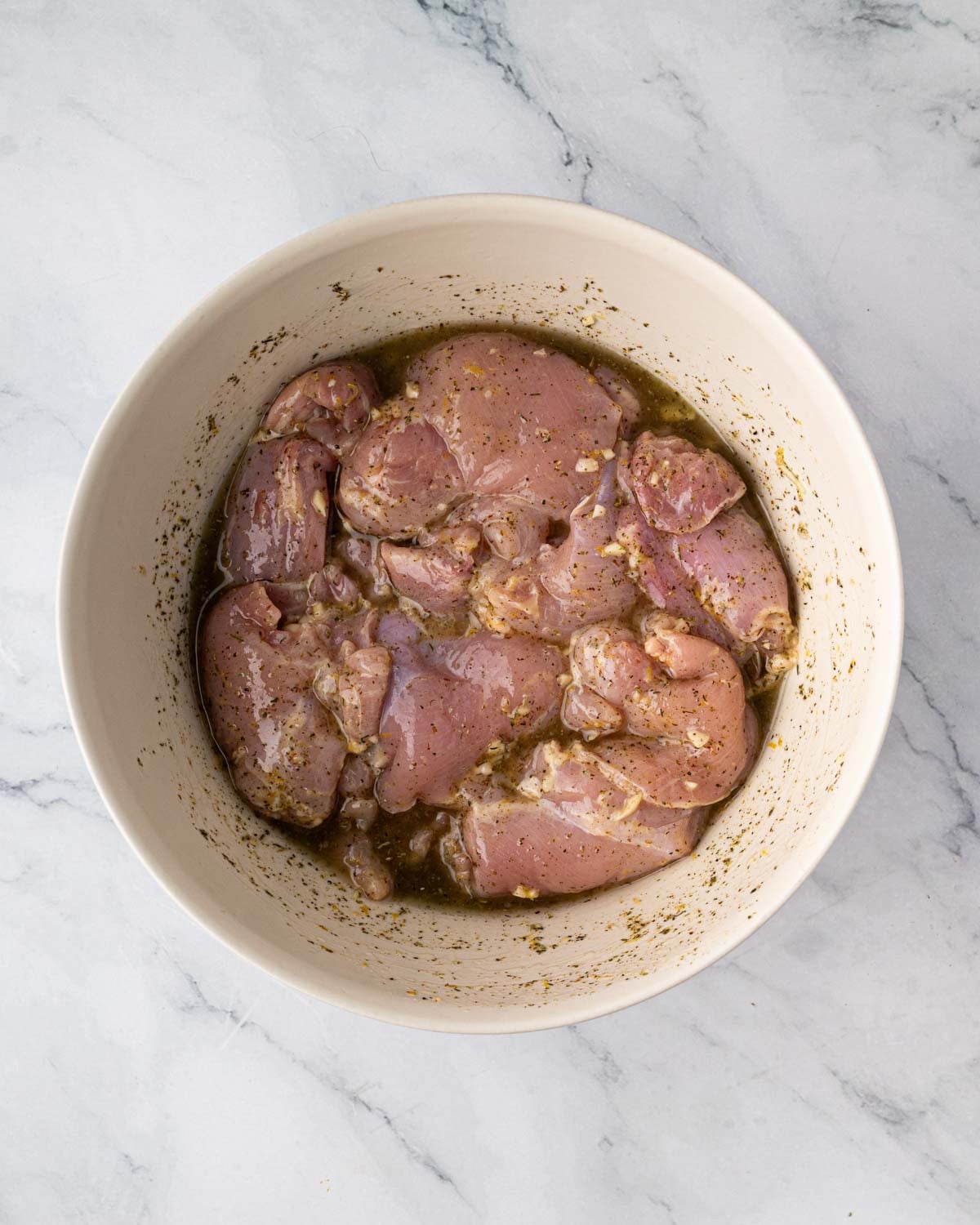 Marinating chicken thighs in a large white bowl in a lemon marinade.