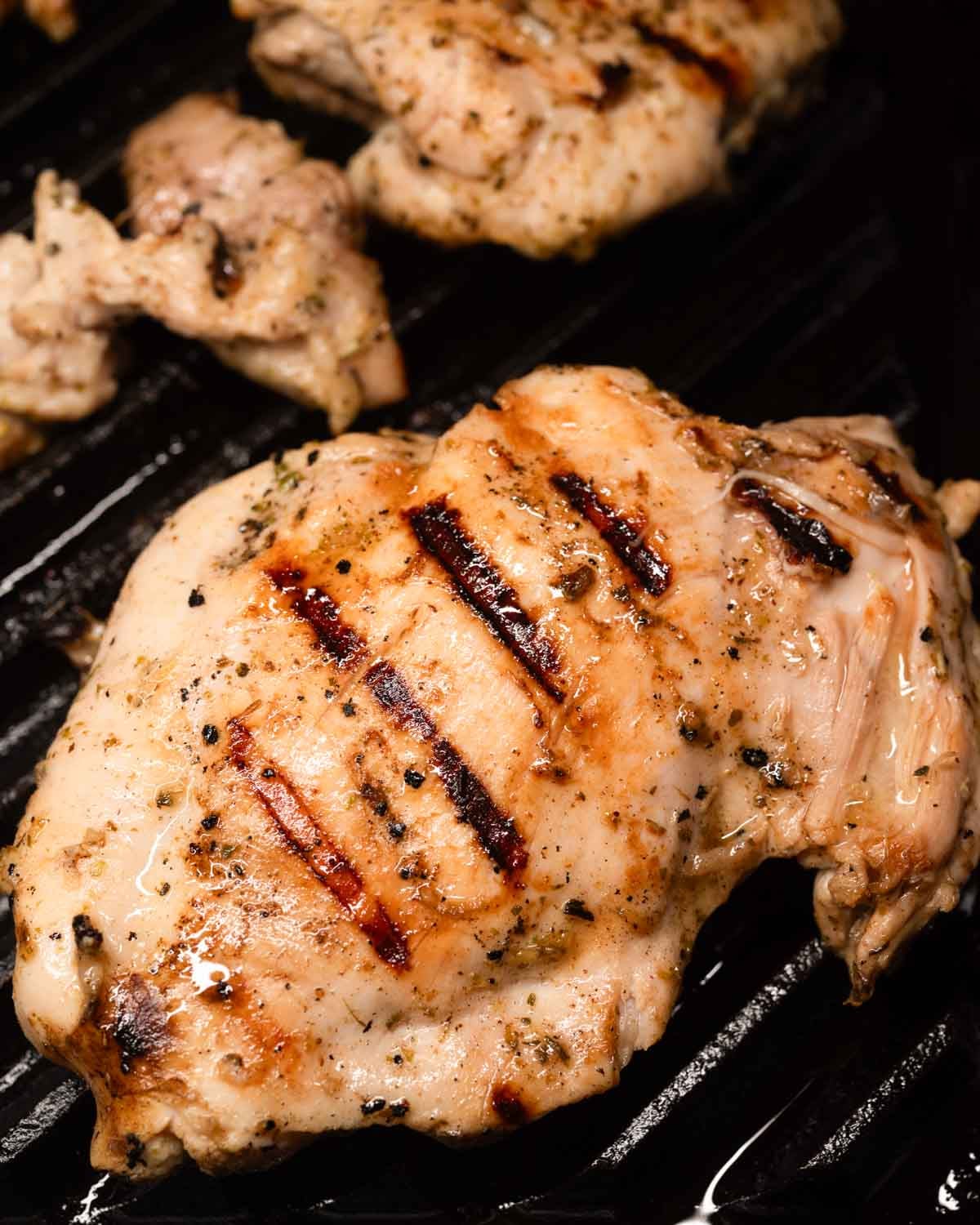 Flipped grilled lemon chicken thighs cooking on the second side on the grill.