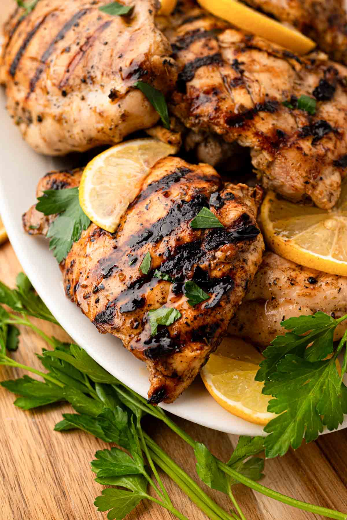 Grilled lemon chicken thighs on a white platter.