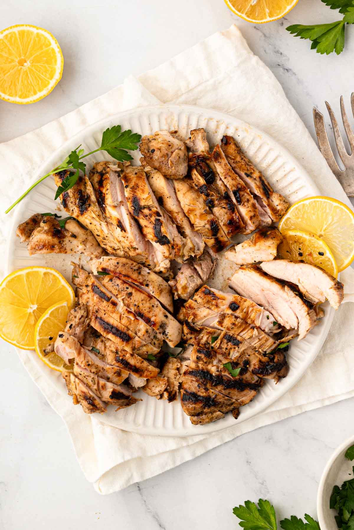 Grilled lemon chicken thighs that are thinly sliced on a white plate with lemon slices.