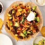 Overhead image of air fryer nachos in parchment paper on a plate with toppings around it.