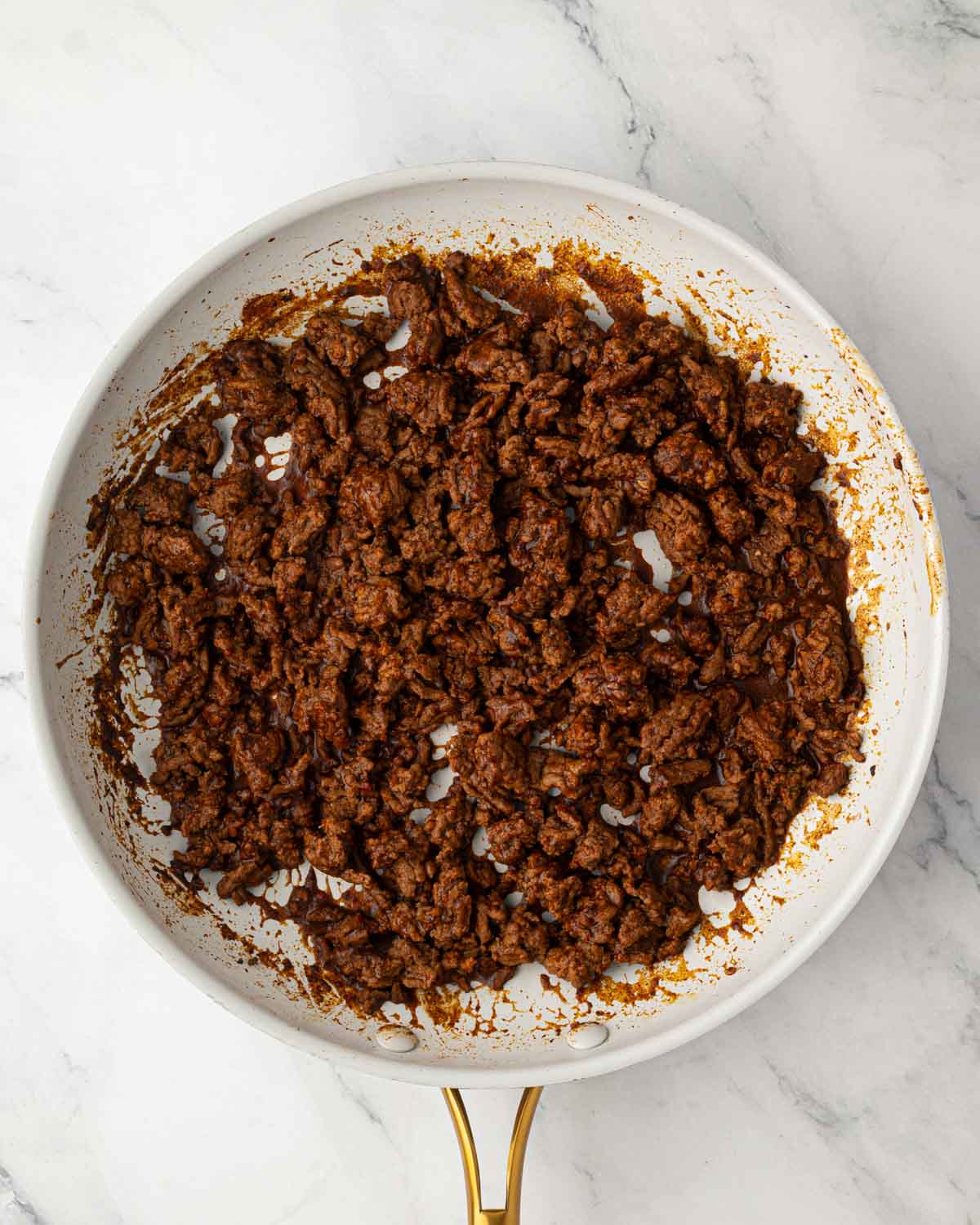 A skillet with ground beef cooking with seasonings.