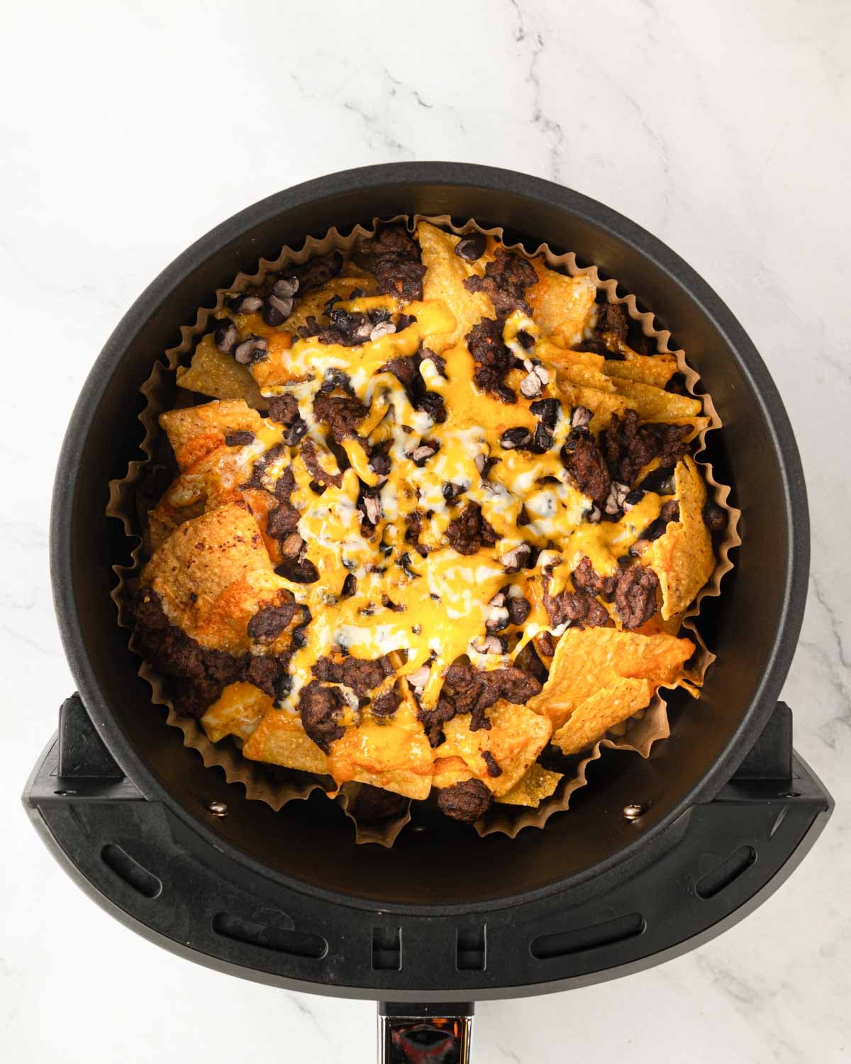 An air fryer basket with parchment liner and cooked air fryer nachos.