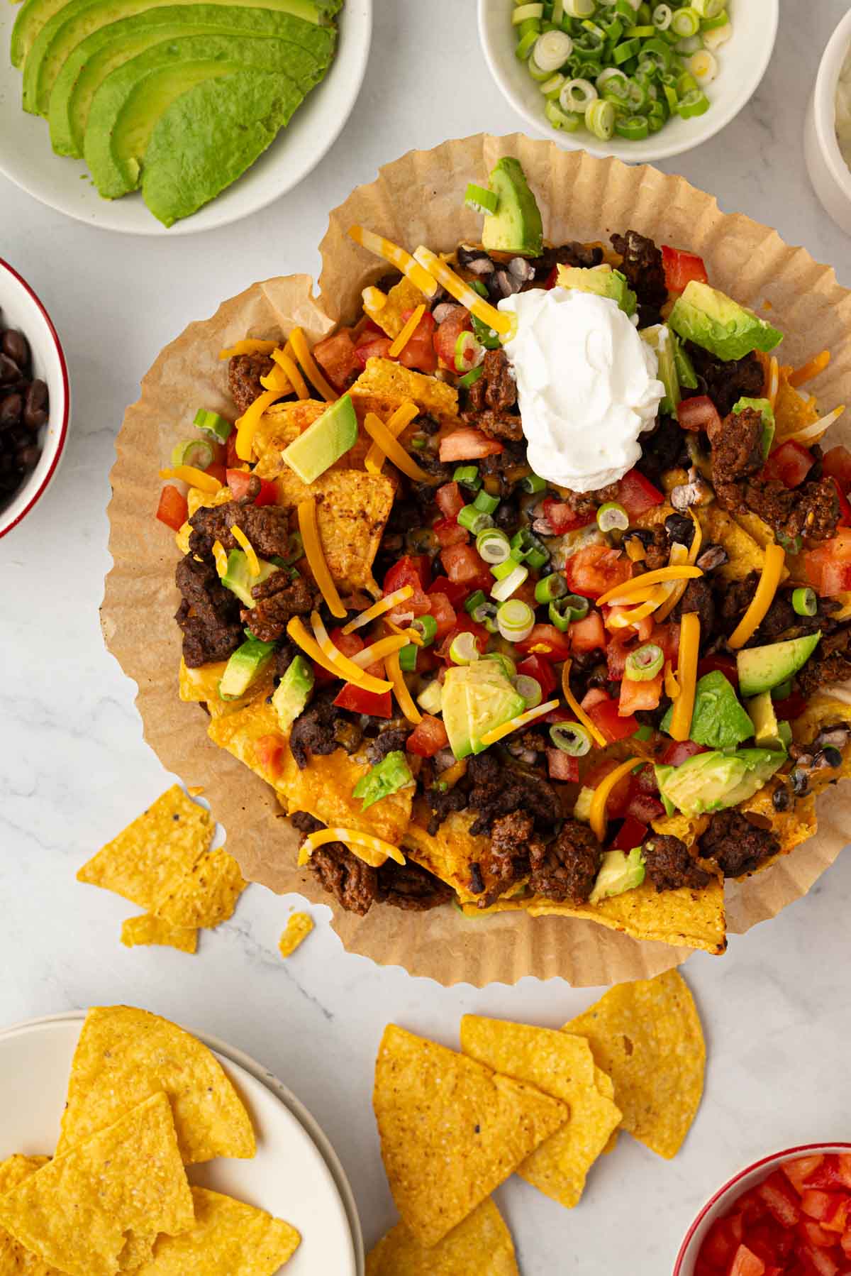 Overhead image of air fryer nachos in a parchment paper liner with toppings around them.