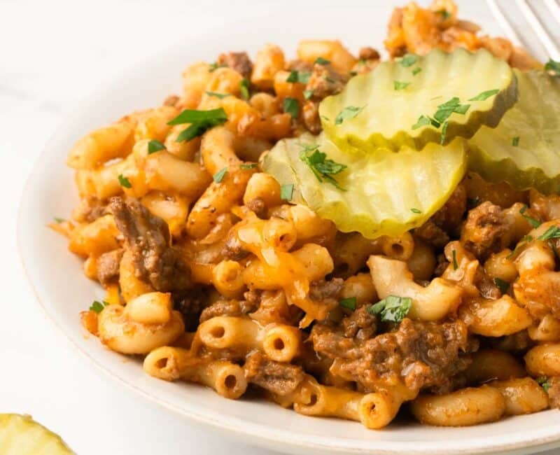 A white plate with cheeseburger pasta with dill pickle slices on top.