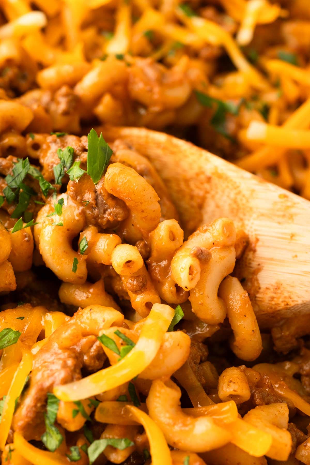 A close up image of a wooden spoon scooping up cheeseburger pasta.