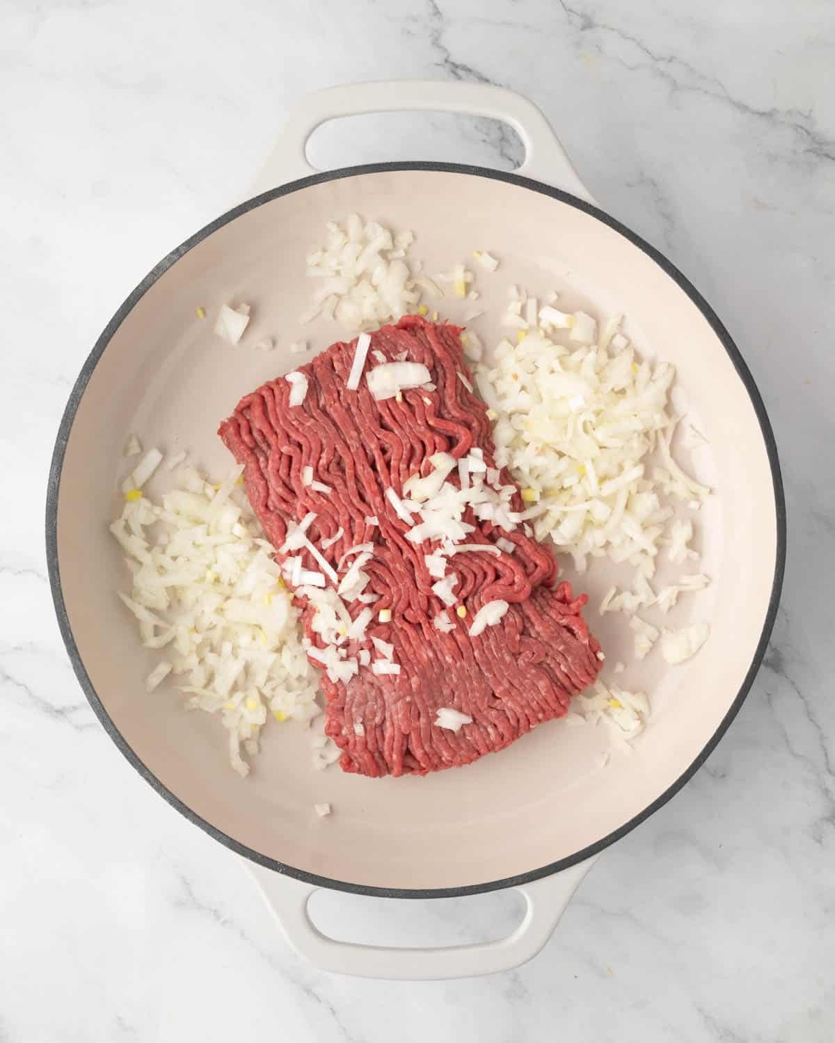 A white skillet with diced onion and ground beef.