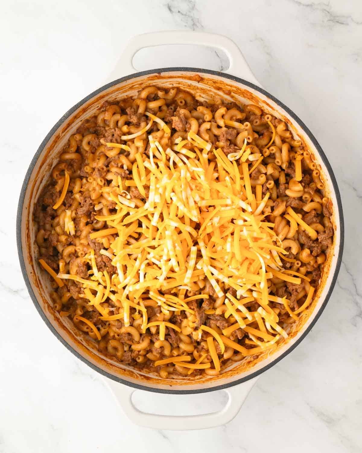 Cooked cheeseburger pasta in a white skillet with shredded cheese on top.