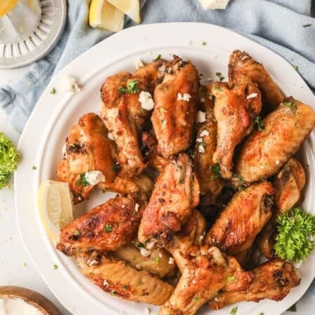 Grilled chicken wings on a white plate with a blue linen underneath.