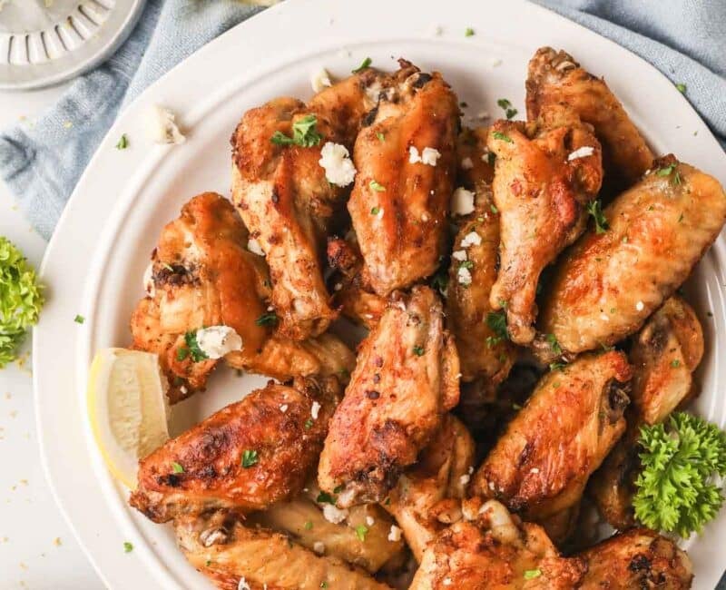 Grilled chicken wings on a white plate with a blue linen underneath.