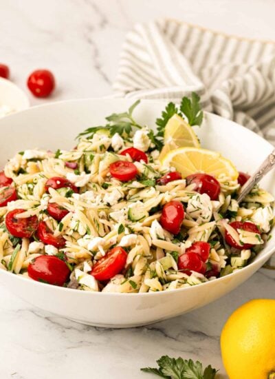 Lemon orzo salad in a white bowl with a spoon and a striped linen in the background.