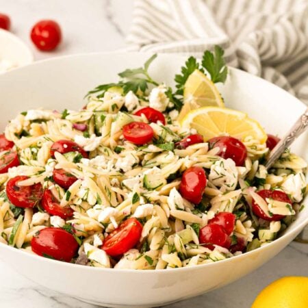 Lemon orzo salad in a white bowl with a spoon and a striped linen in the background.