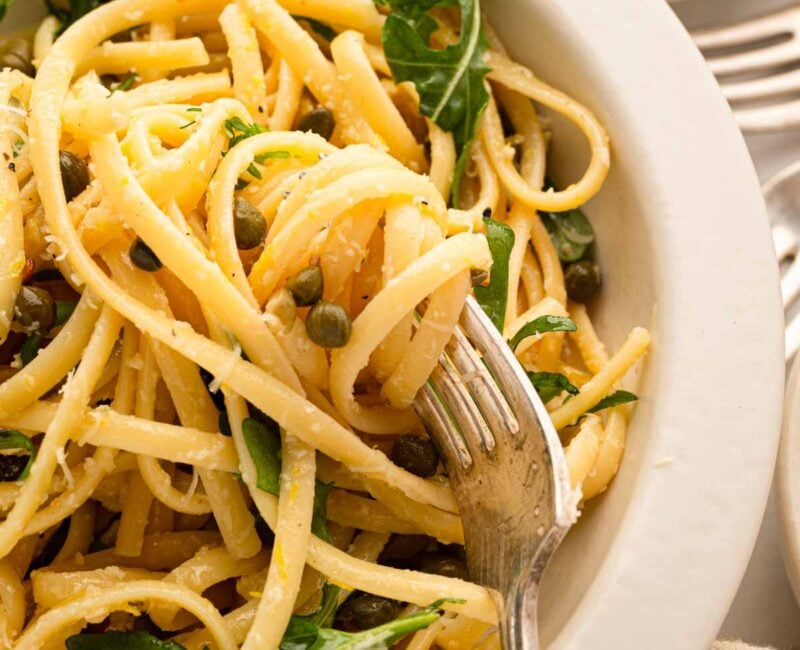 A white bowl with lemon caper pasta.