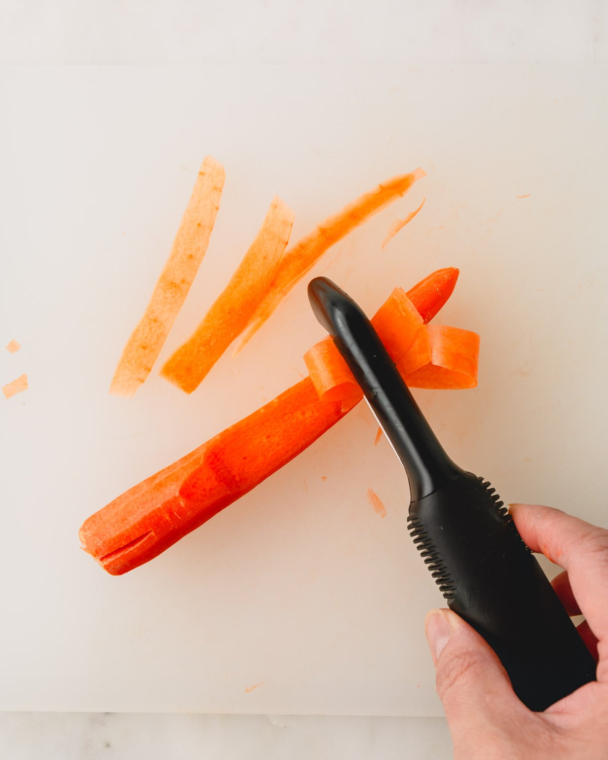 A peeler is making carrot ribbons on a cutting board.
