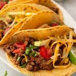 Ground beef tacos resting on a white platter.