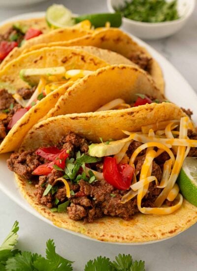 Ground beef tacos resting on a white platter.