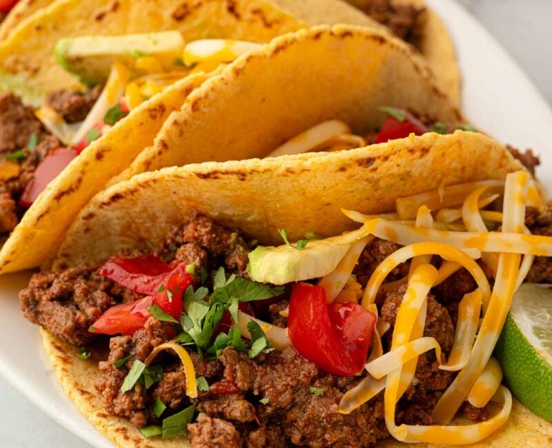 Ground beef tacos resting on a white platter.
