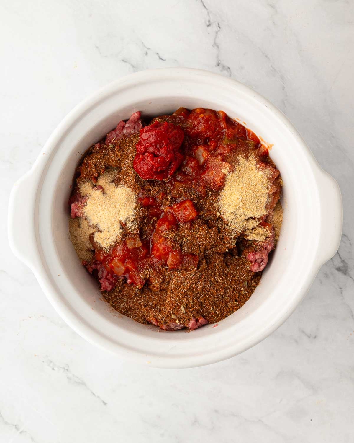 Ingredients for slow cooker ground beef tacos in a white slow cooker.