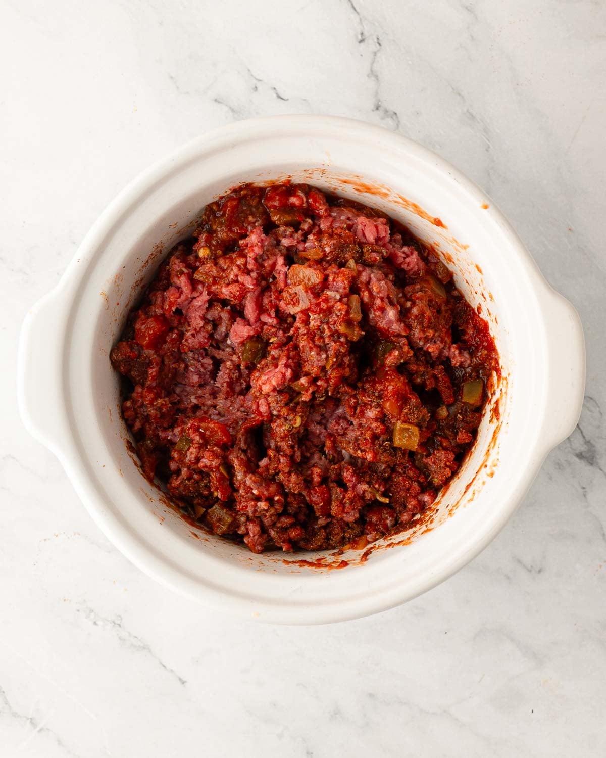 Ingredients mixed for slow cooker ground beef tacos in a white crock pot.