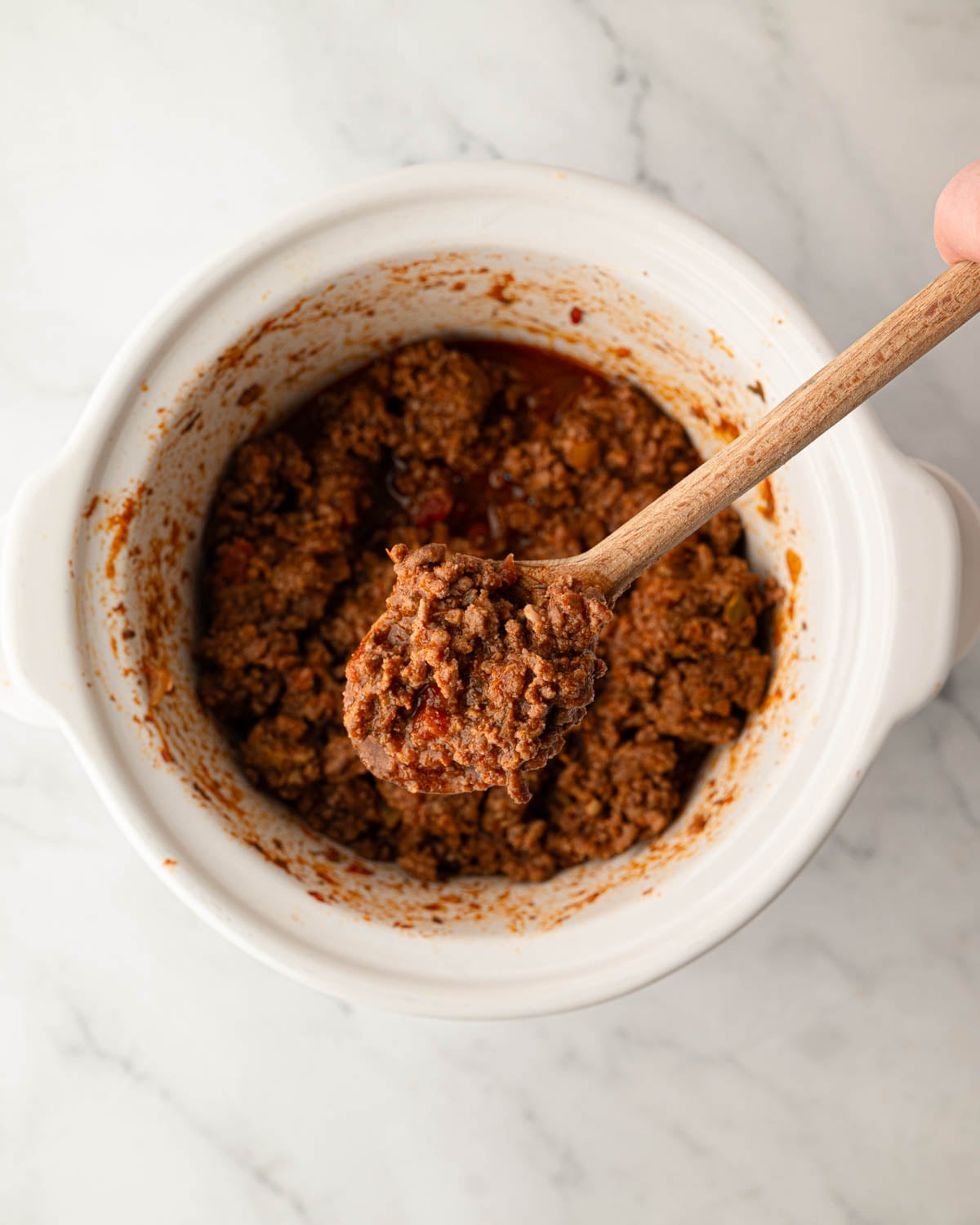 A slow cooker with a wooden spoon scooping up ground beef taco meat.