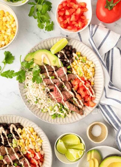 Steak bowl in a white plate with small white bowls of other ingredients to the side. A second steak bowl is partially shown in the bottom left corner.