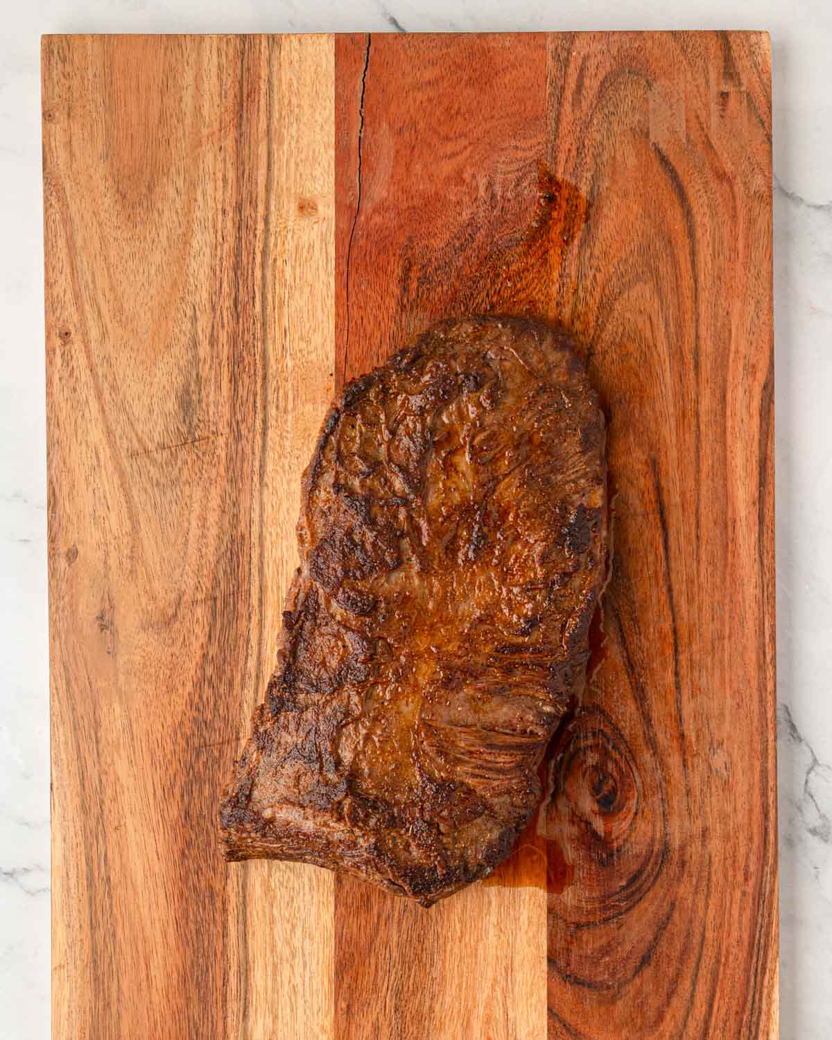 A wooden cutting board with a steak resting on it.