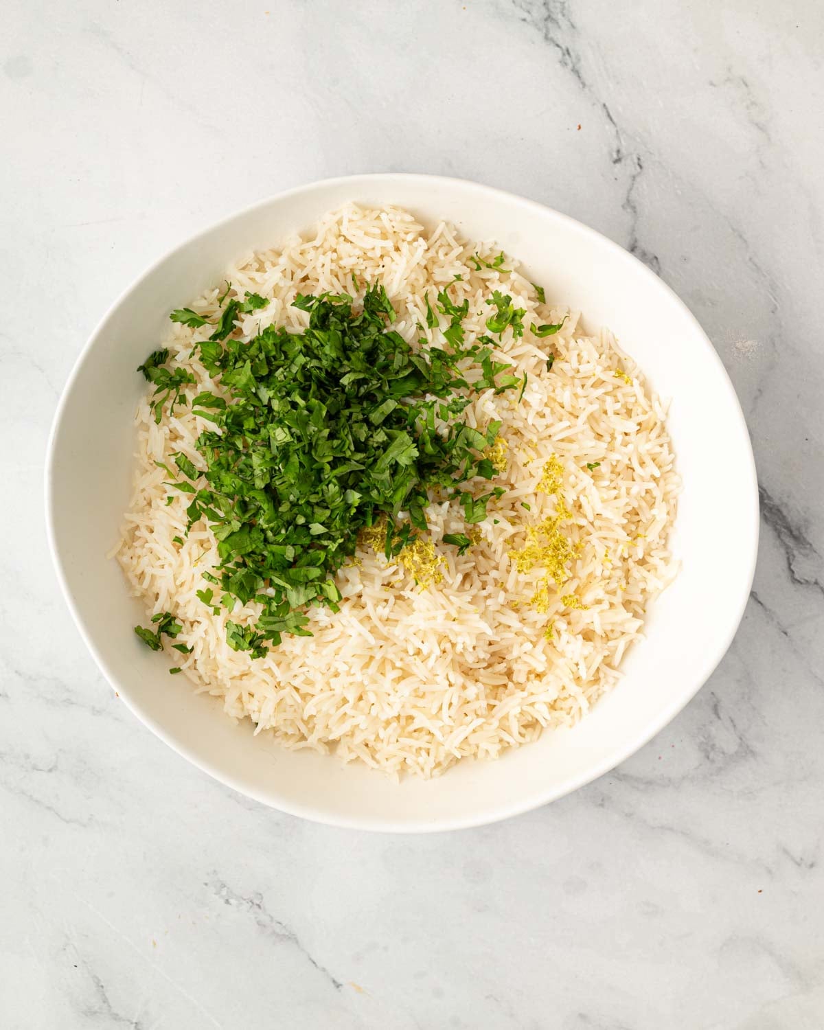 A white bowl with cooked rice, oil, and chopped herbs.