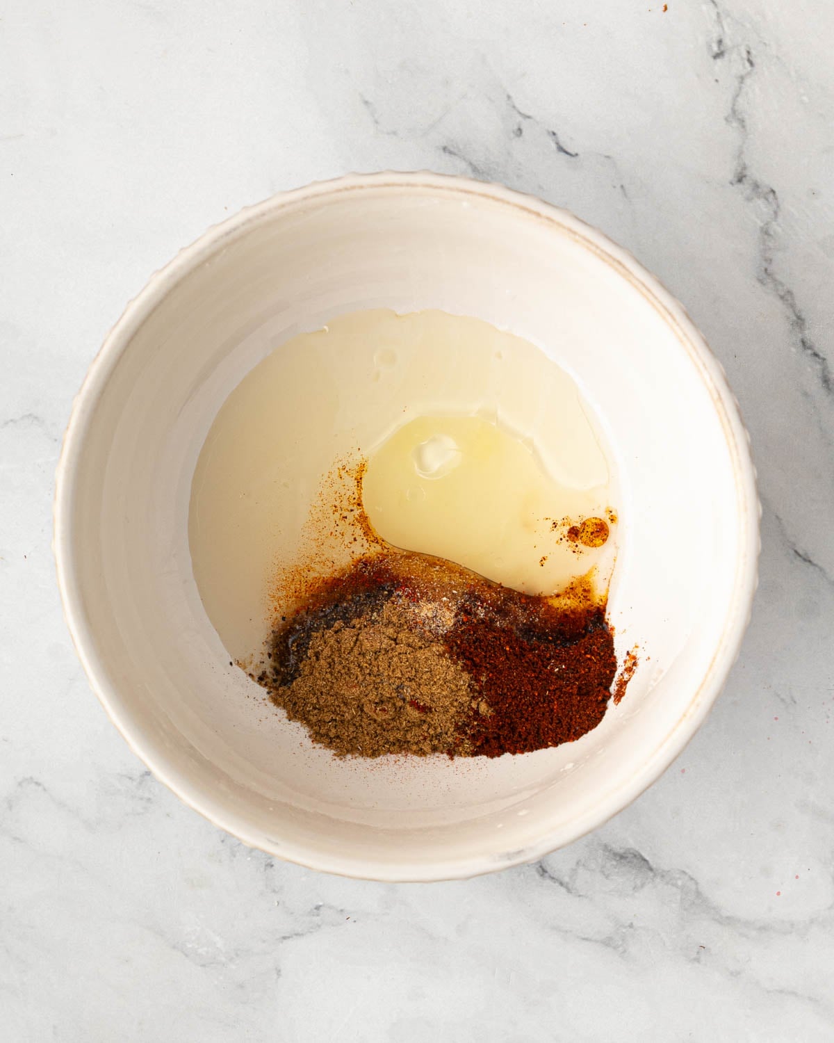 A white bowl with spices and oil.