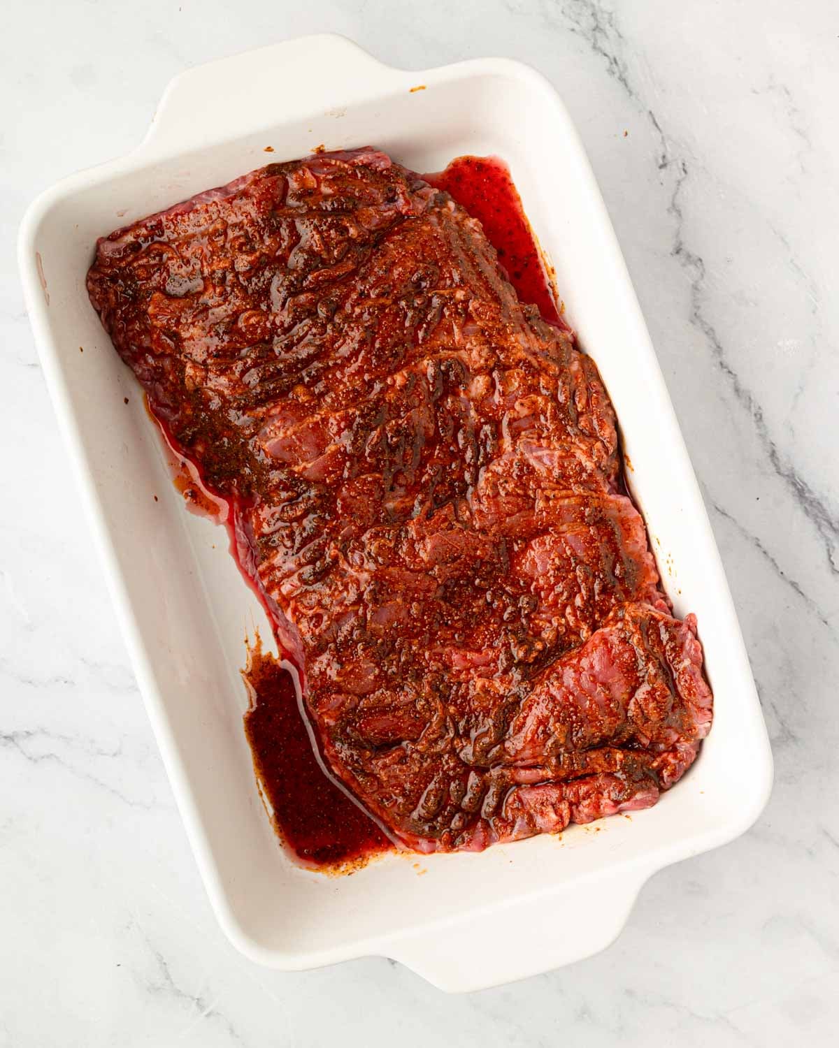 A white baking dish with steak and the marinade.